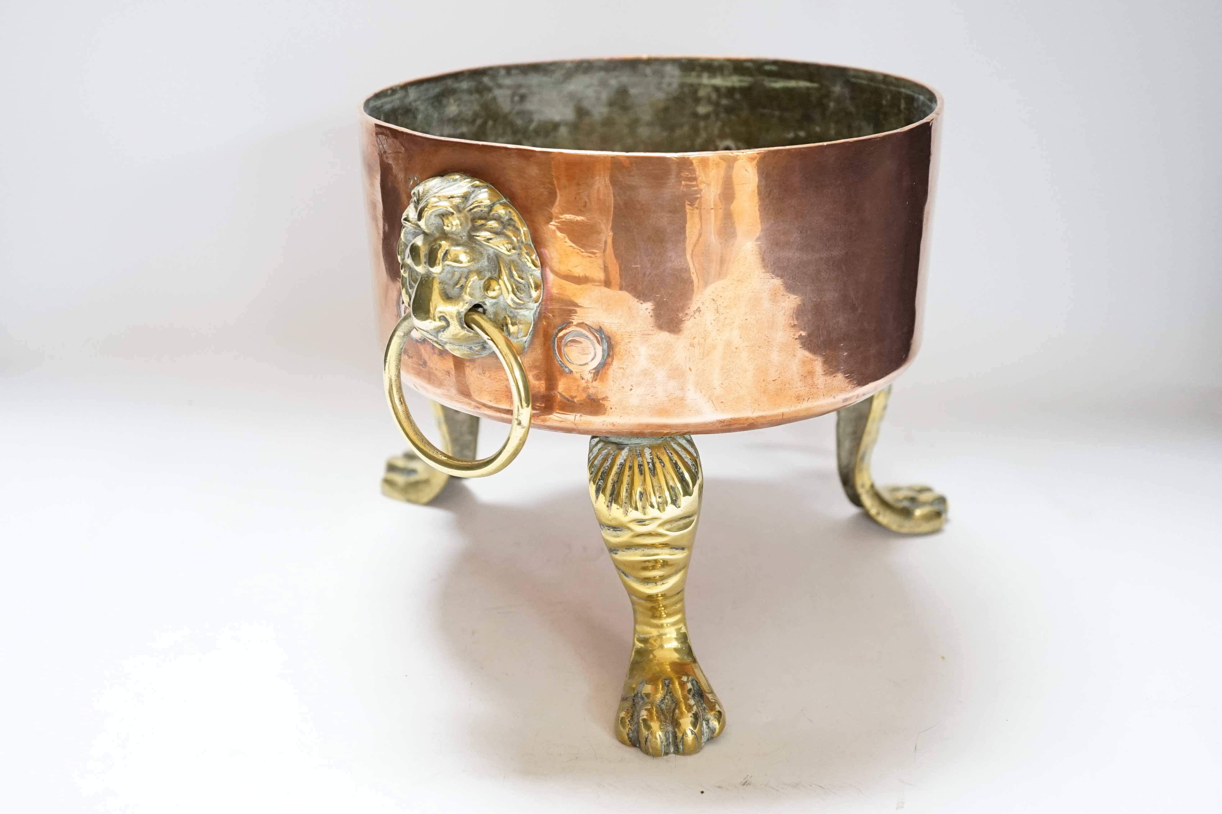 A heavy copper planter or cooking pot, with cast brass lion mask and ring handles, on brass claw feet, 20cm high